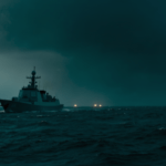 Illustrazione atmosferica notturna di una nave militare al largo della costa con luci misteriose sospese sull'oceano, a rappresentare il caso UAP indagato dal Pentagono
