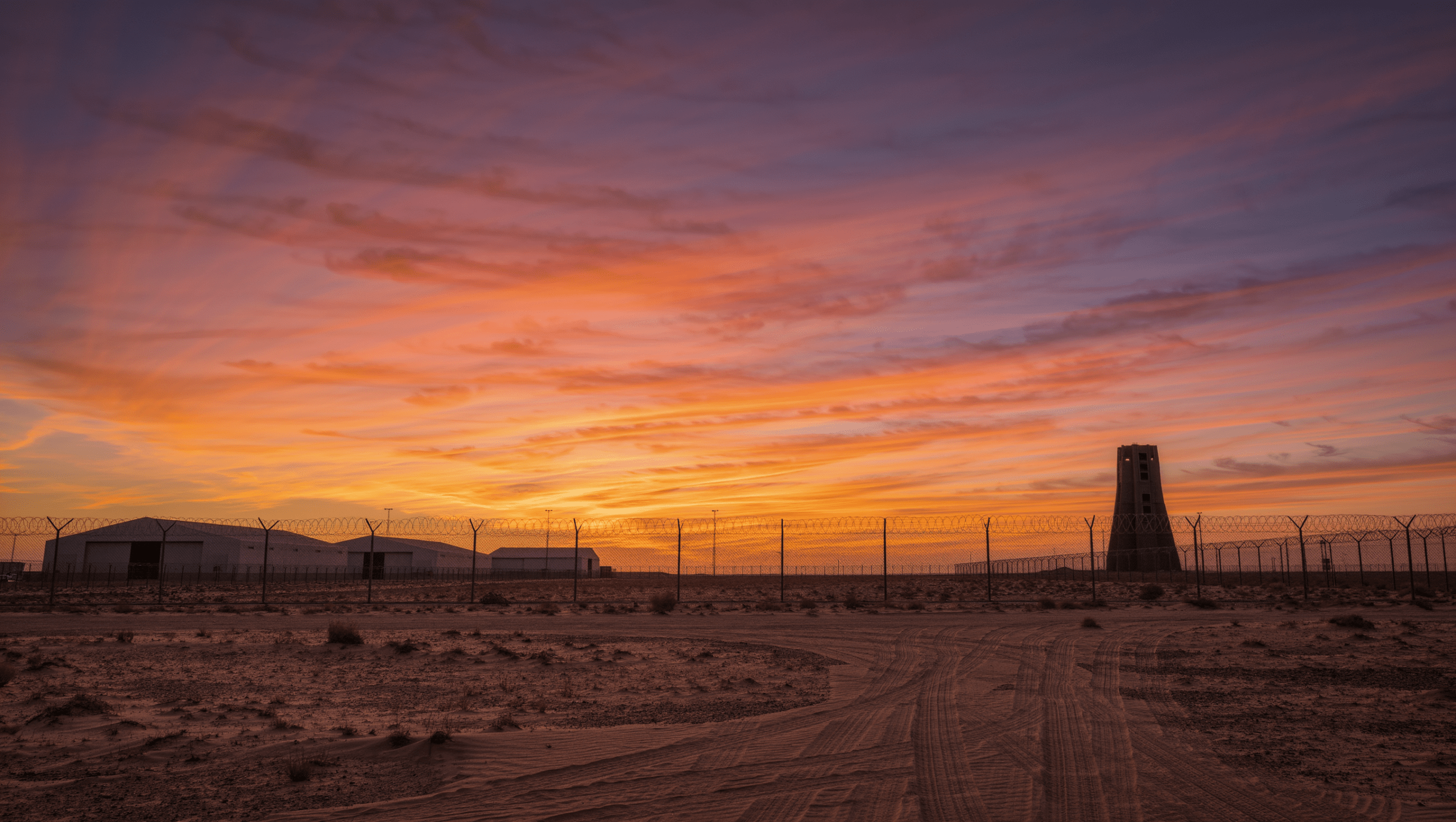 Base militare remota nel deserto con torre misteriosa all'orizzonte